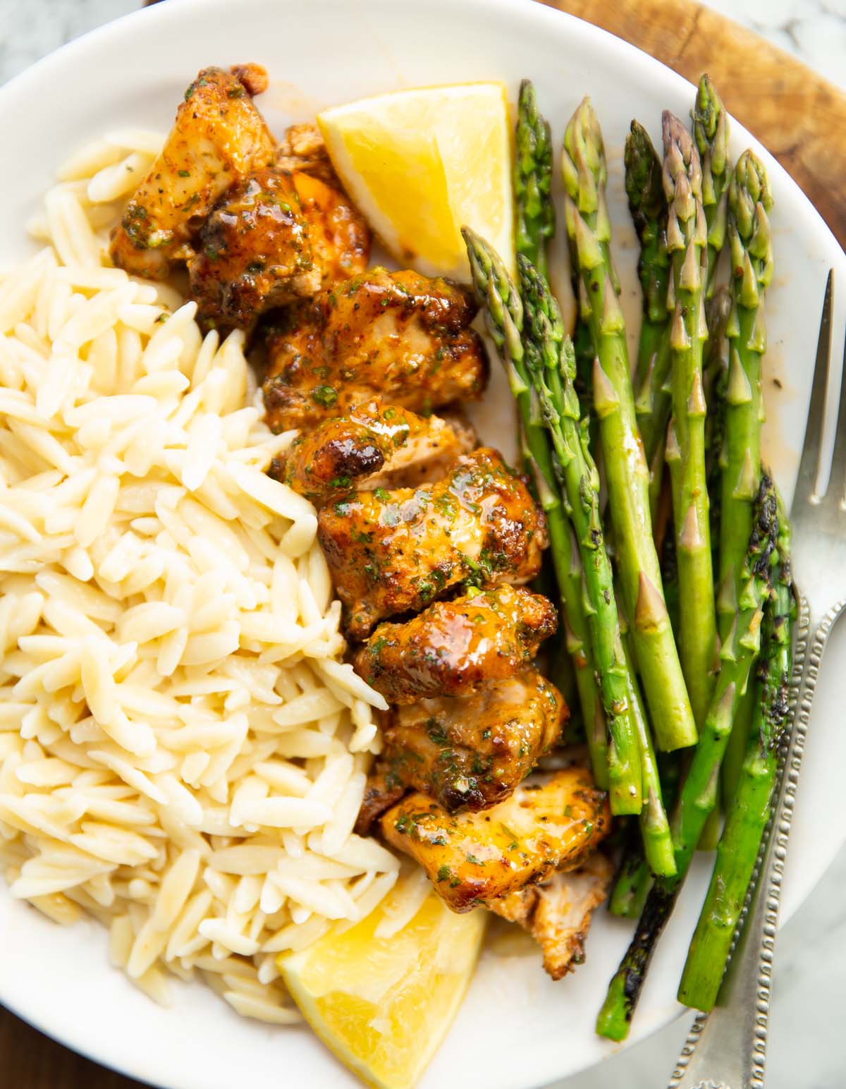 overhead shot of lemon butter chicken on small white plate with orzo and asparagus