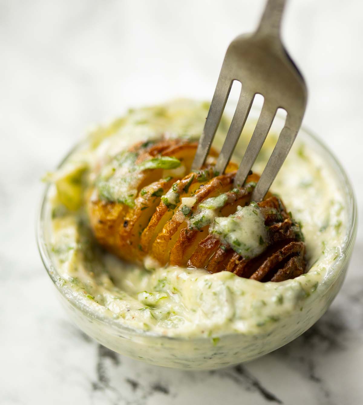 silver fork dunking potato into glass pot of garlic butter
