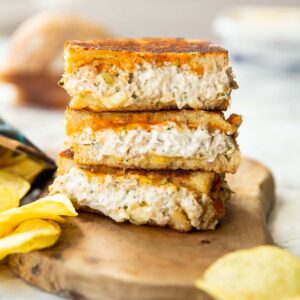 3 tuna melt halves stacked on each other on wooden chopping board with crisps