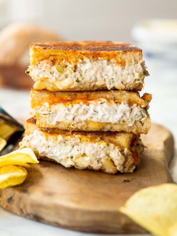 3 tuna melt halves stacked on each other on wooden chopping board with crisps