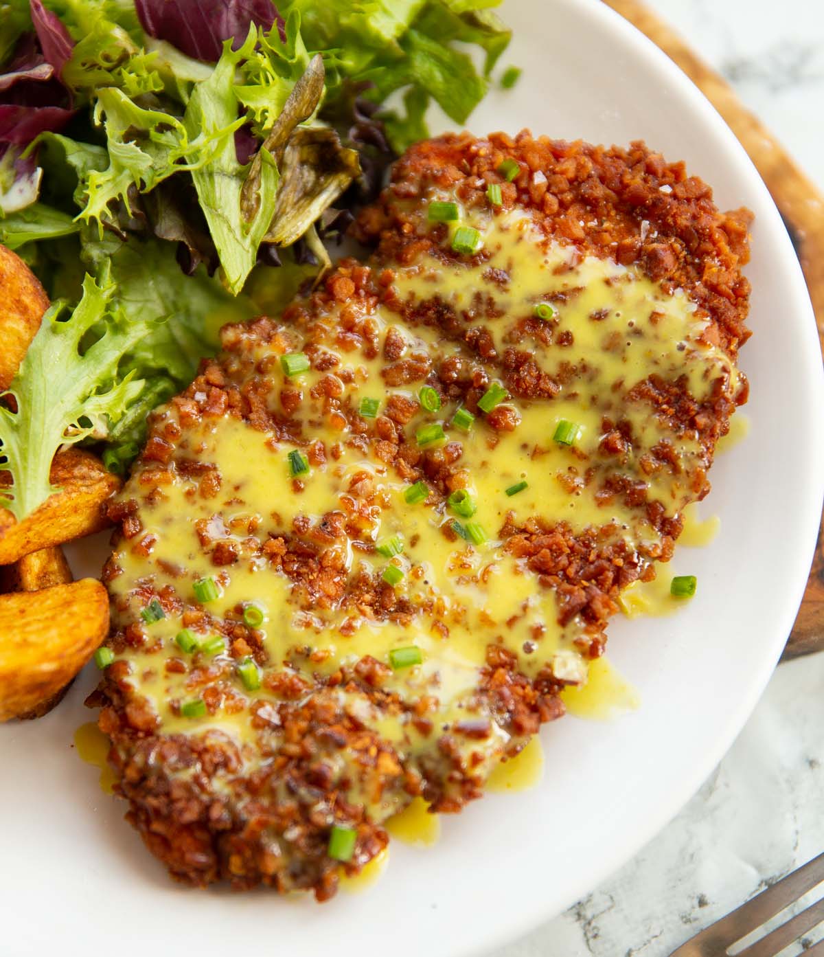 close up shot of pretzel crusted chicken on honey mustard sauce on small white plate
