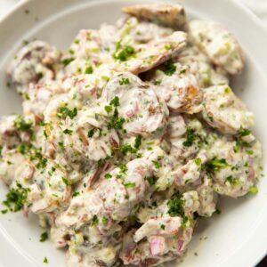 smashed potato salad in large white bowl garnished with parsley