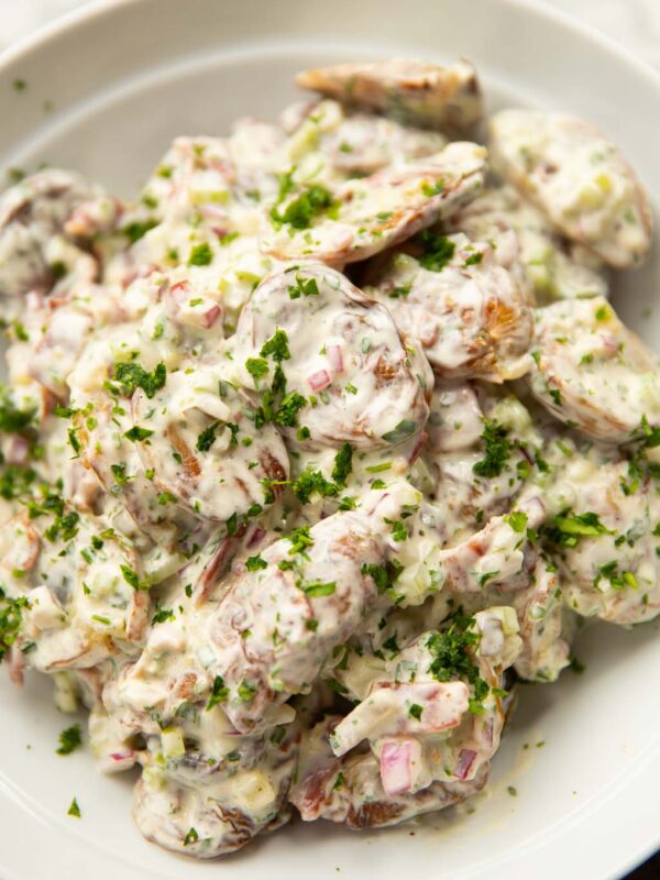 smashed potato salad in large white bowl garnished with parsley