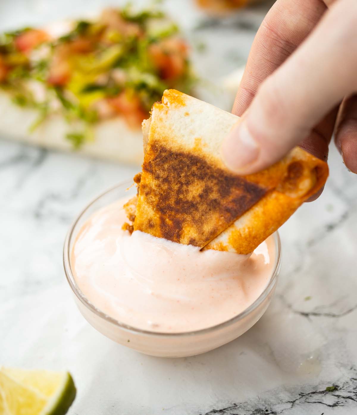 hand dunking half a taco pocket into small glass pot of dip