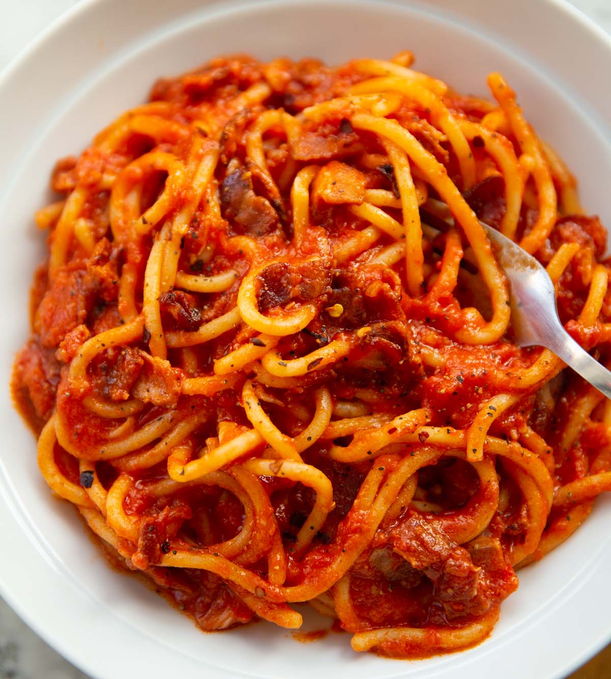 close up shot of tomato and bacon pasta in large white dish