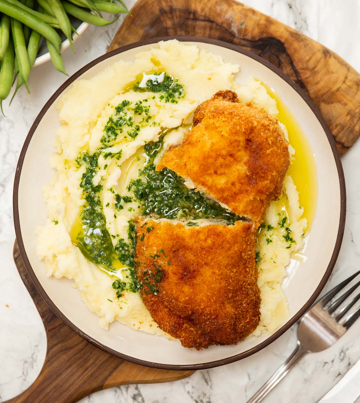 overhead shot of chicken kyiv on bed of mashed potato on small white plate