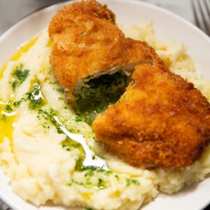chicken kyiv halved on top mashed potato with garlic butter pouring out