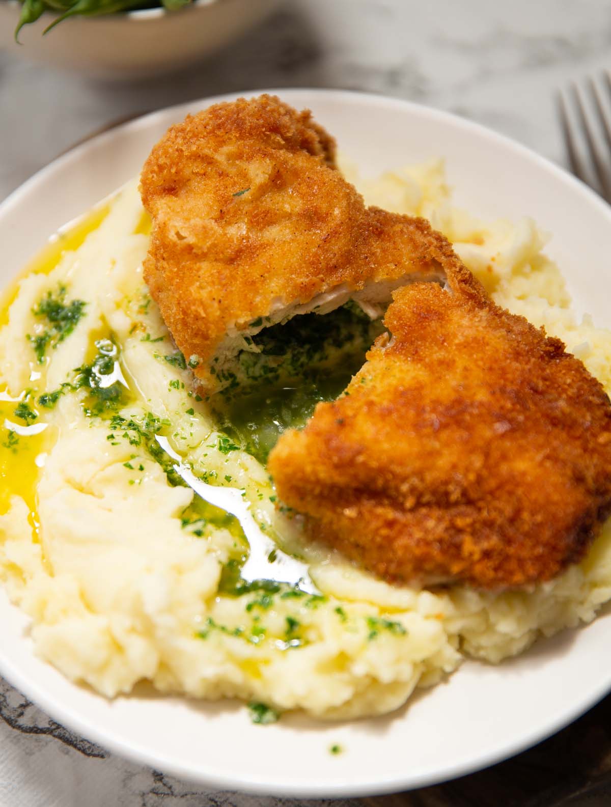 chicken kyiv halved on top mashed potato with garlic butter pouring out