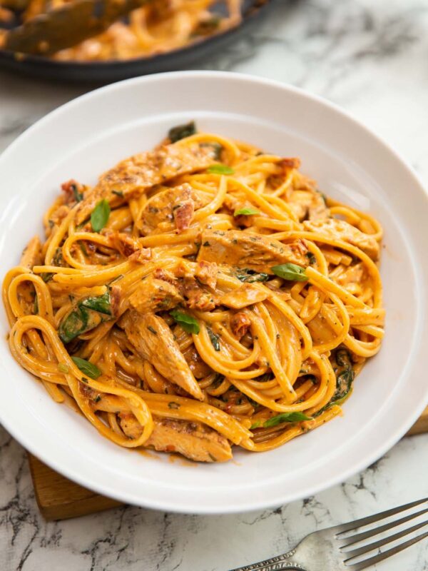 creamy tuscan chicken pasta served in large white bowl on wooden board