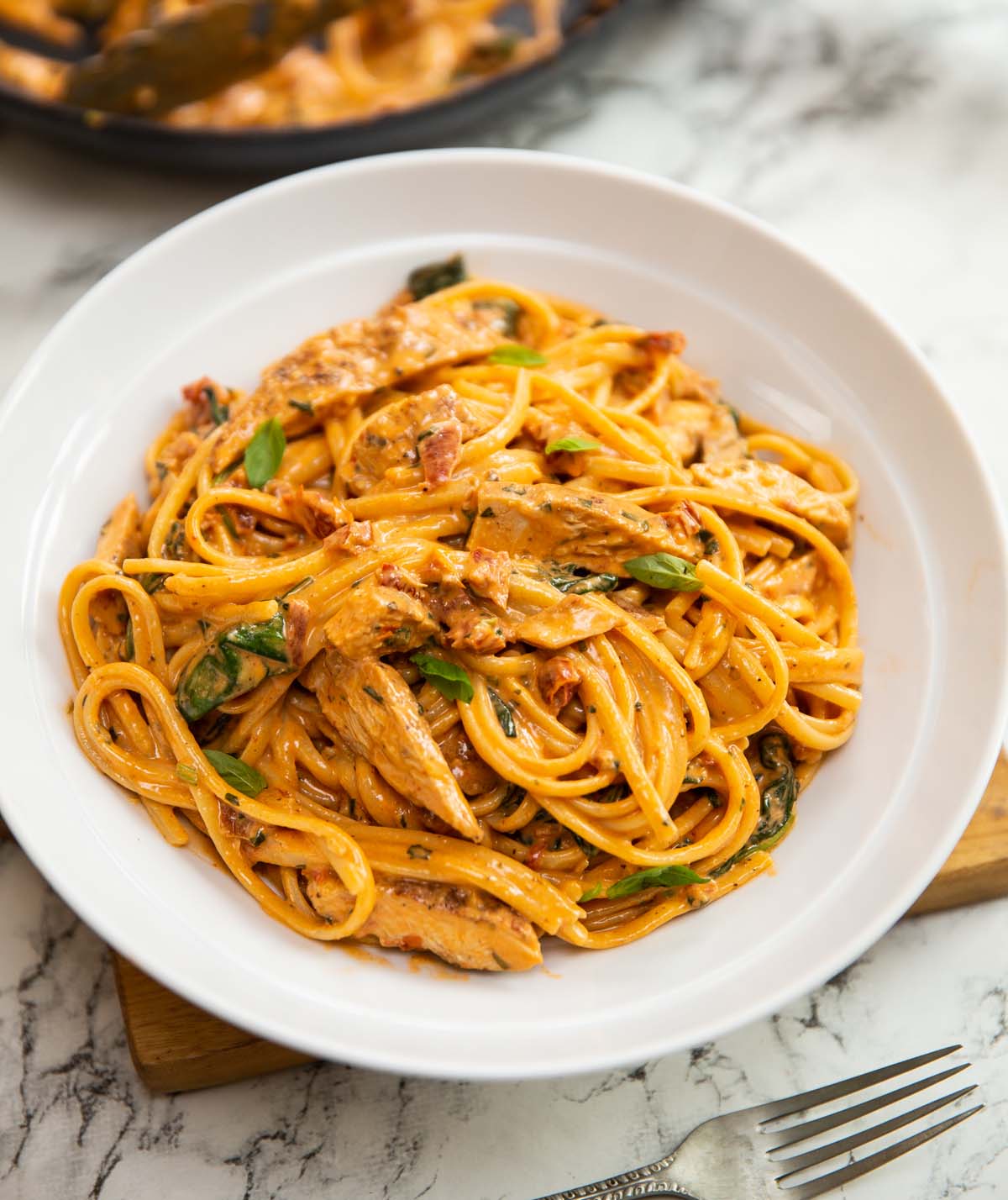 creamy tuscan chicken pasta served in large white bowl on wooden board
