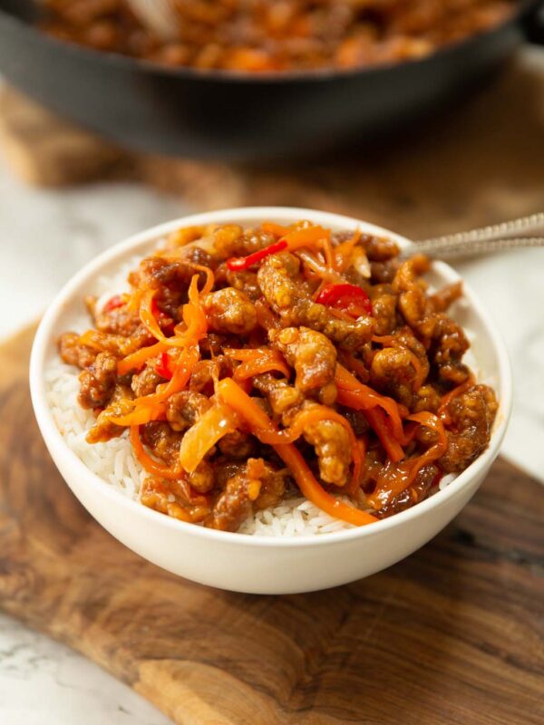 crispy chilli beef served over rice in small white bowl on chopping board