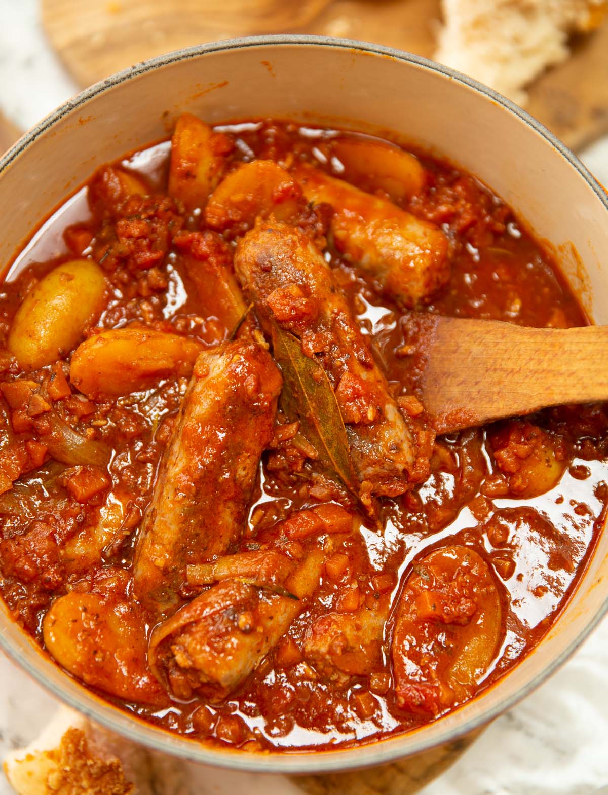overhead shot of hearty sausage casserole in pot with wooden spoon digging in
