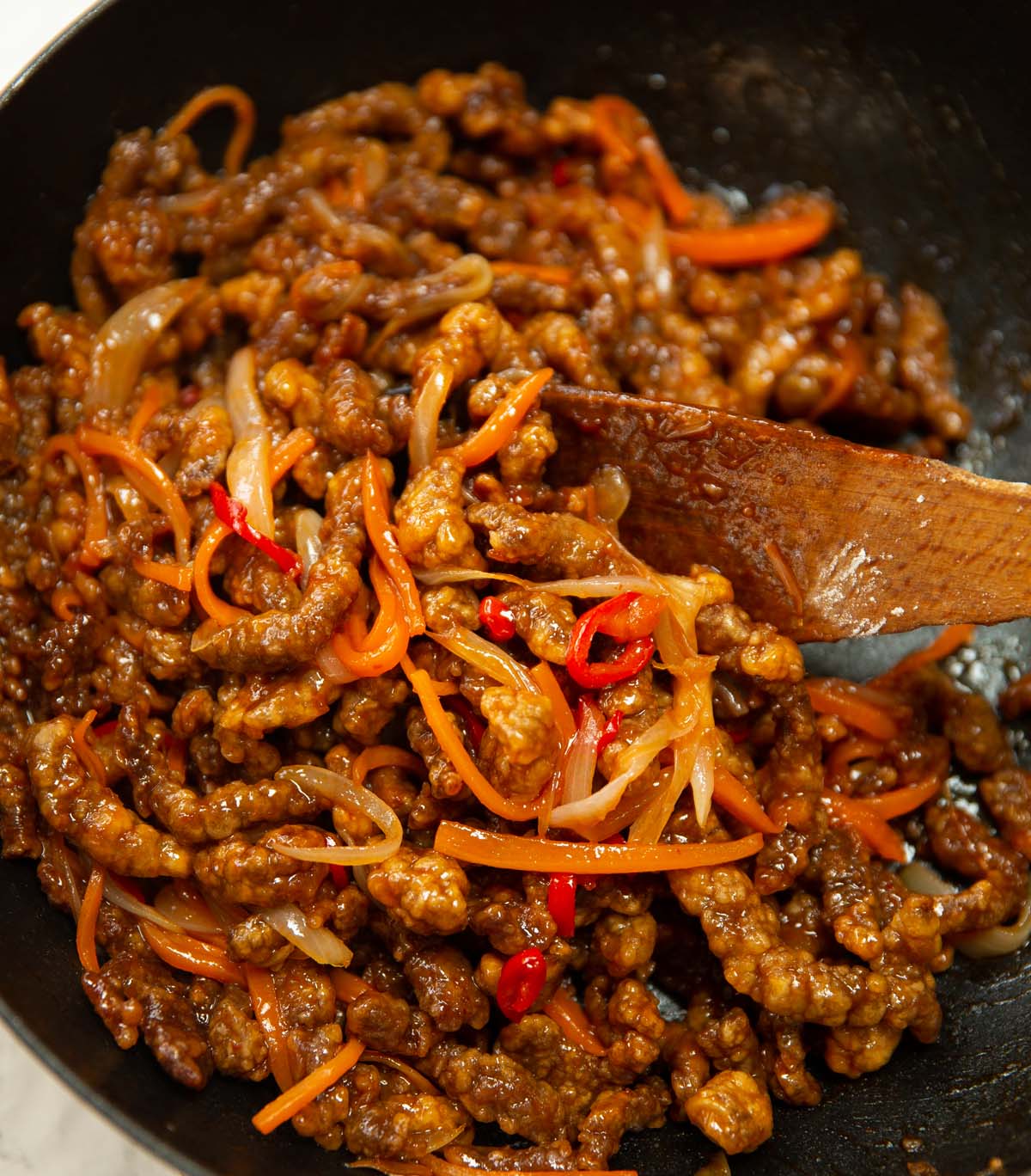 homemade crispy chilli beef in wok with wooden spoon