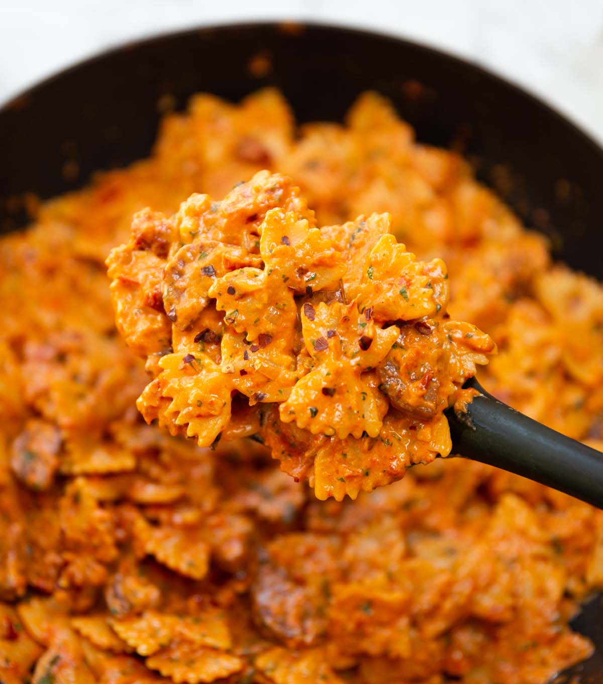 black serving spoon holding portion of spicy chorizo pasta
