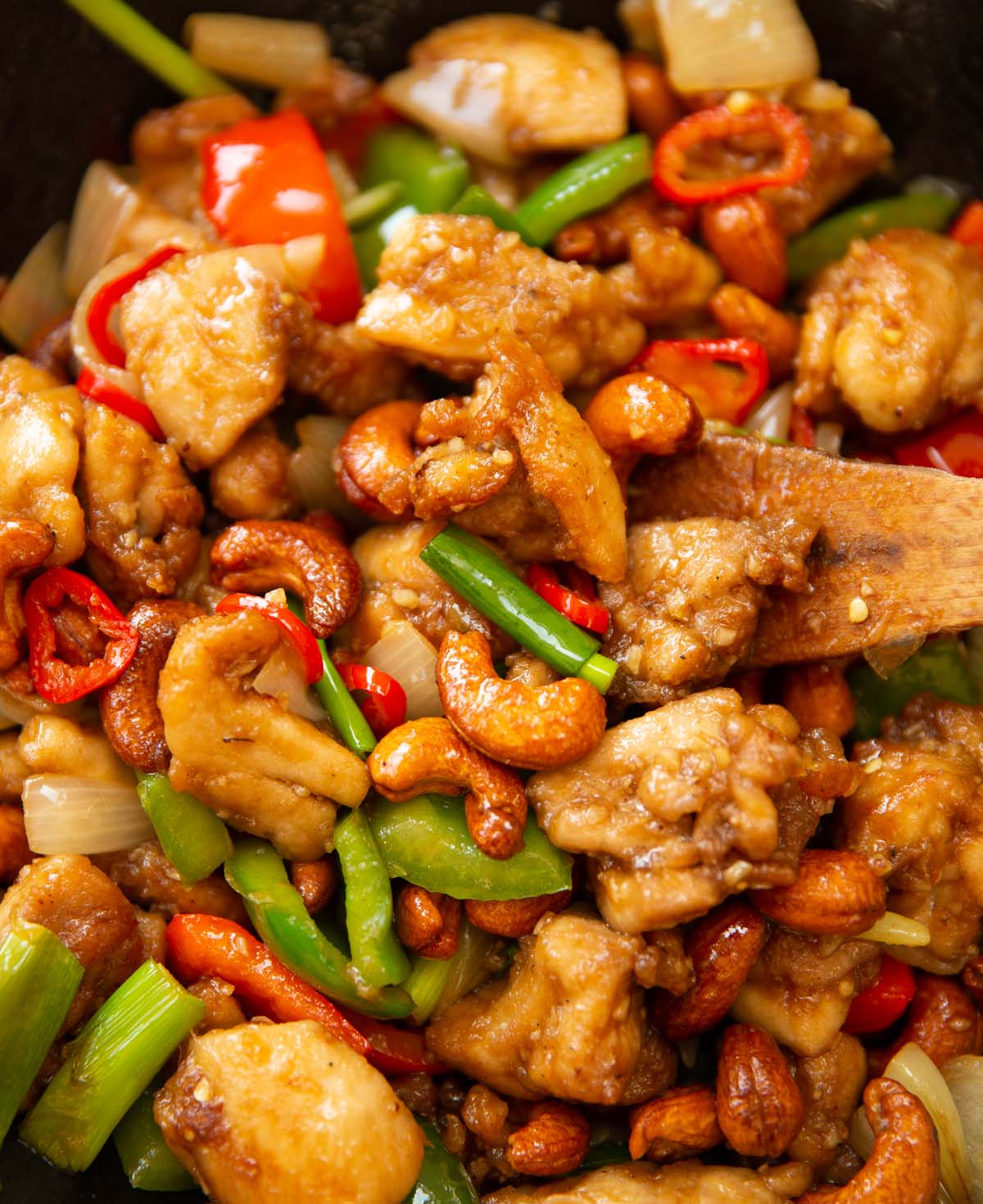 close up shot of Thai cashew chicken in wok with wooden spoon