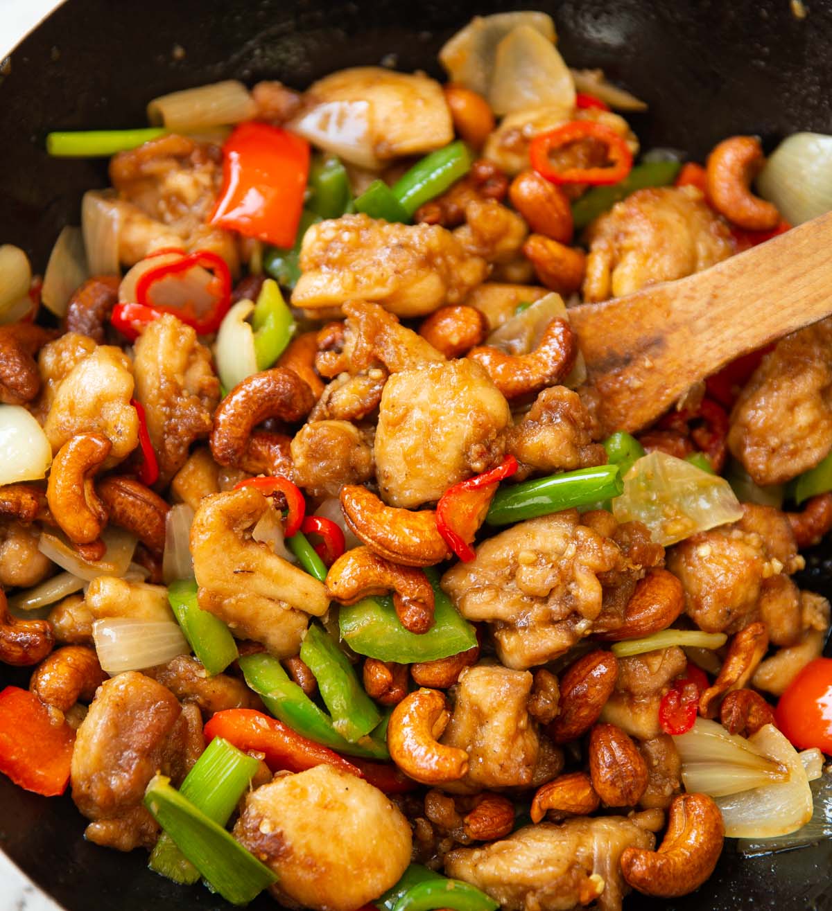 Thai chicken with cashews in wok with wooden spoon digging in