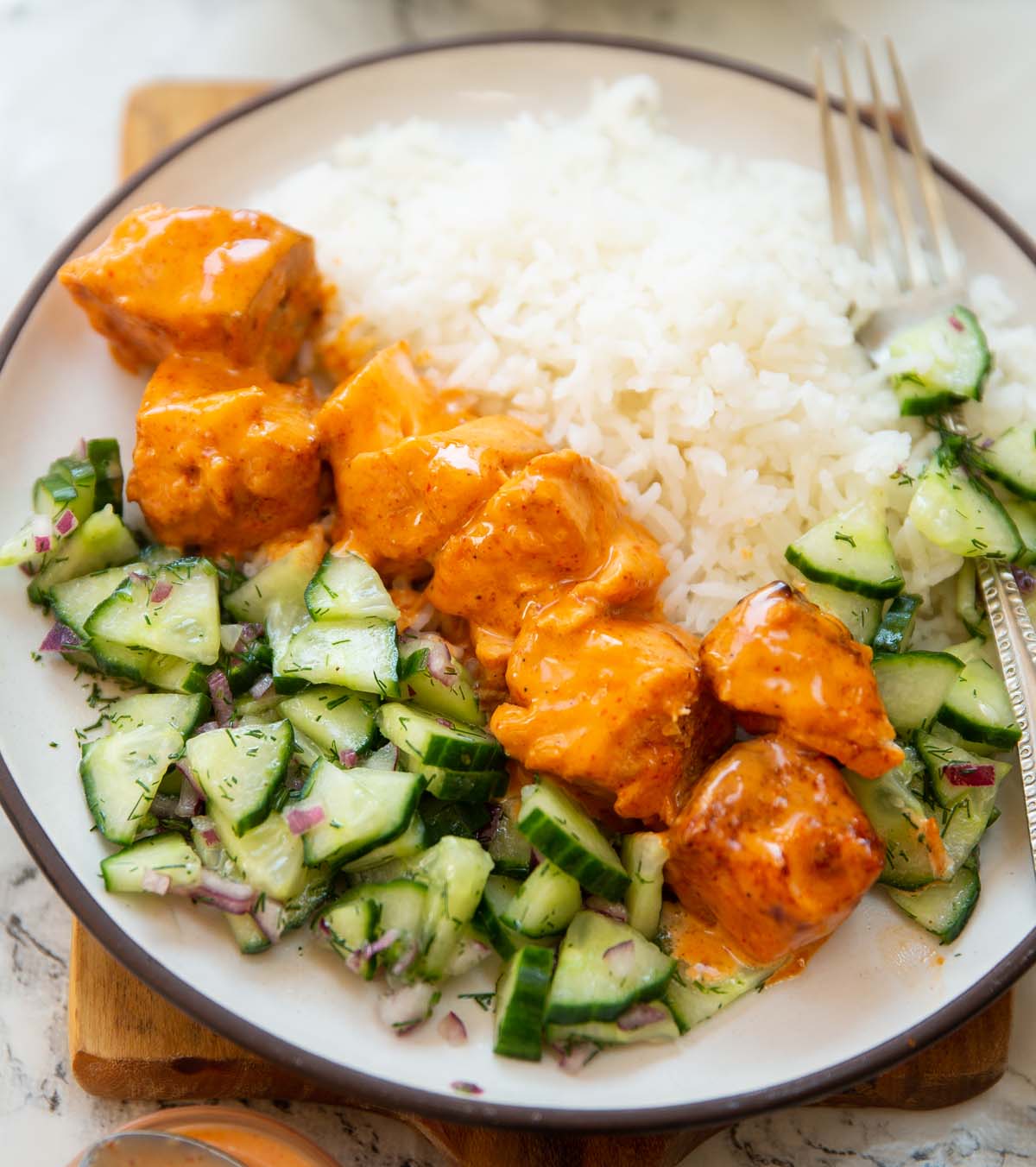 bang bang salmon skewers served on small white plate with rice and cucumber salad