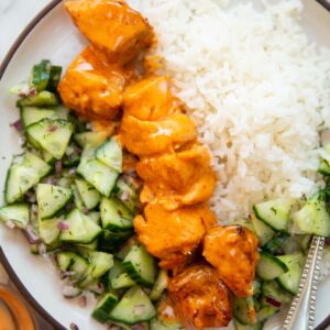 overhead shot of bang bang salmon skewers with rice and cucumber salad