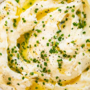 close up shot of creamy mashed potato in dish garnished with chives and melted butter