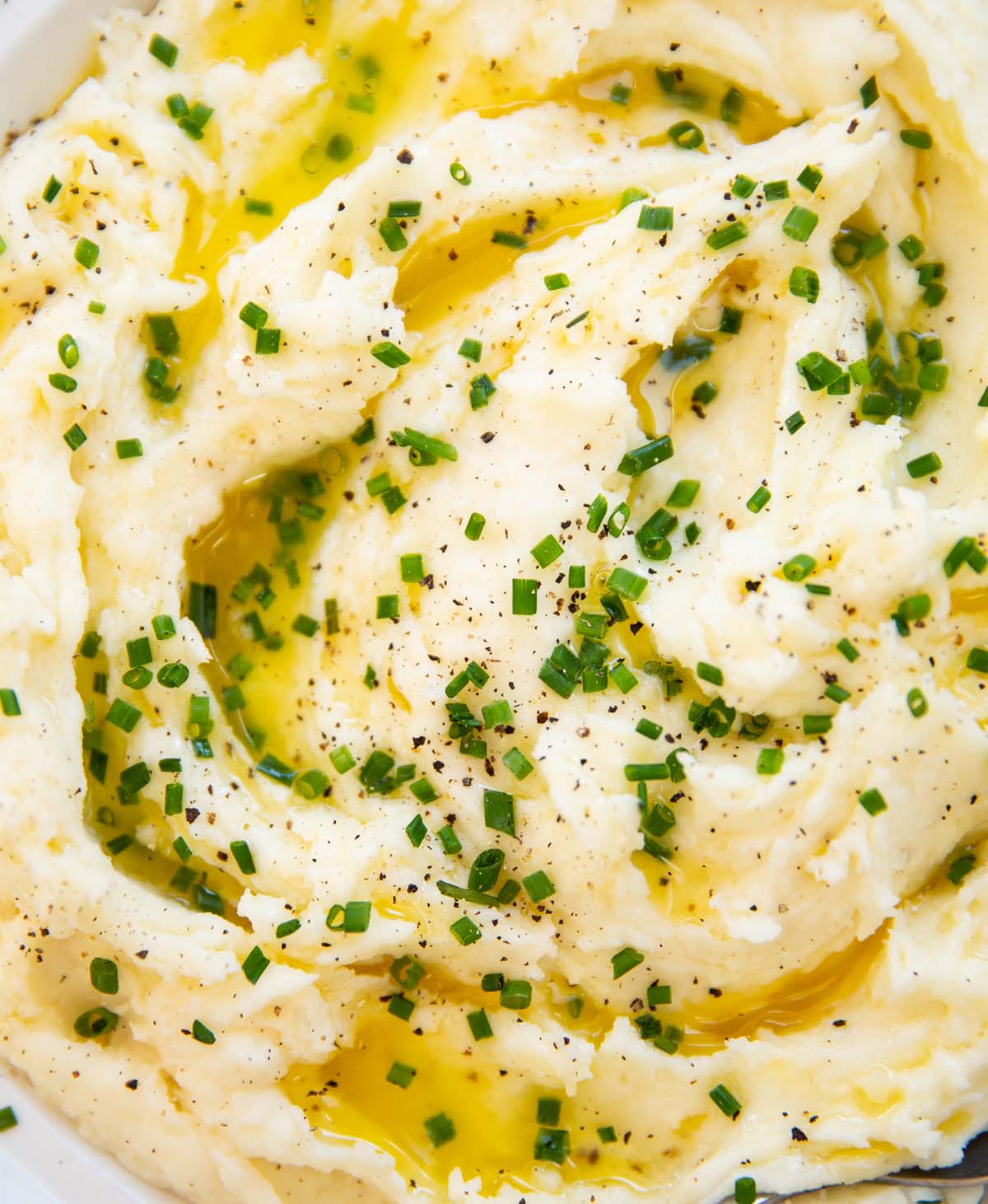 close up shot of creamy mashed potato in dish garnished with chives and melted butter