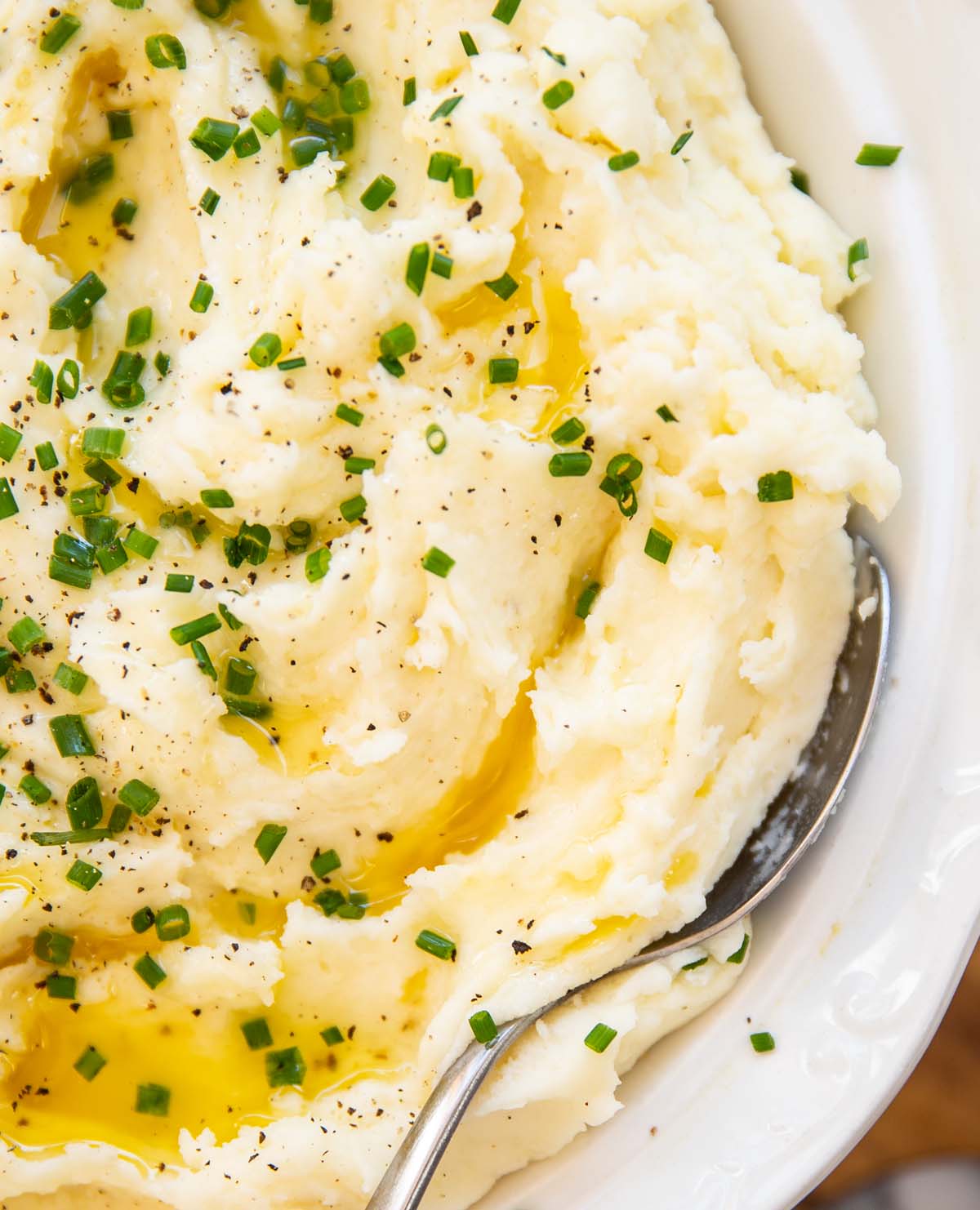 close up shot of silver spoon digging into bowl of creamy mashed potatoes