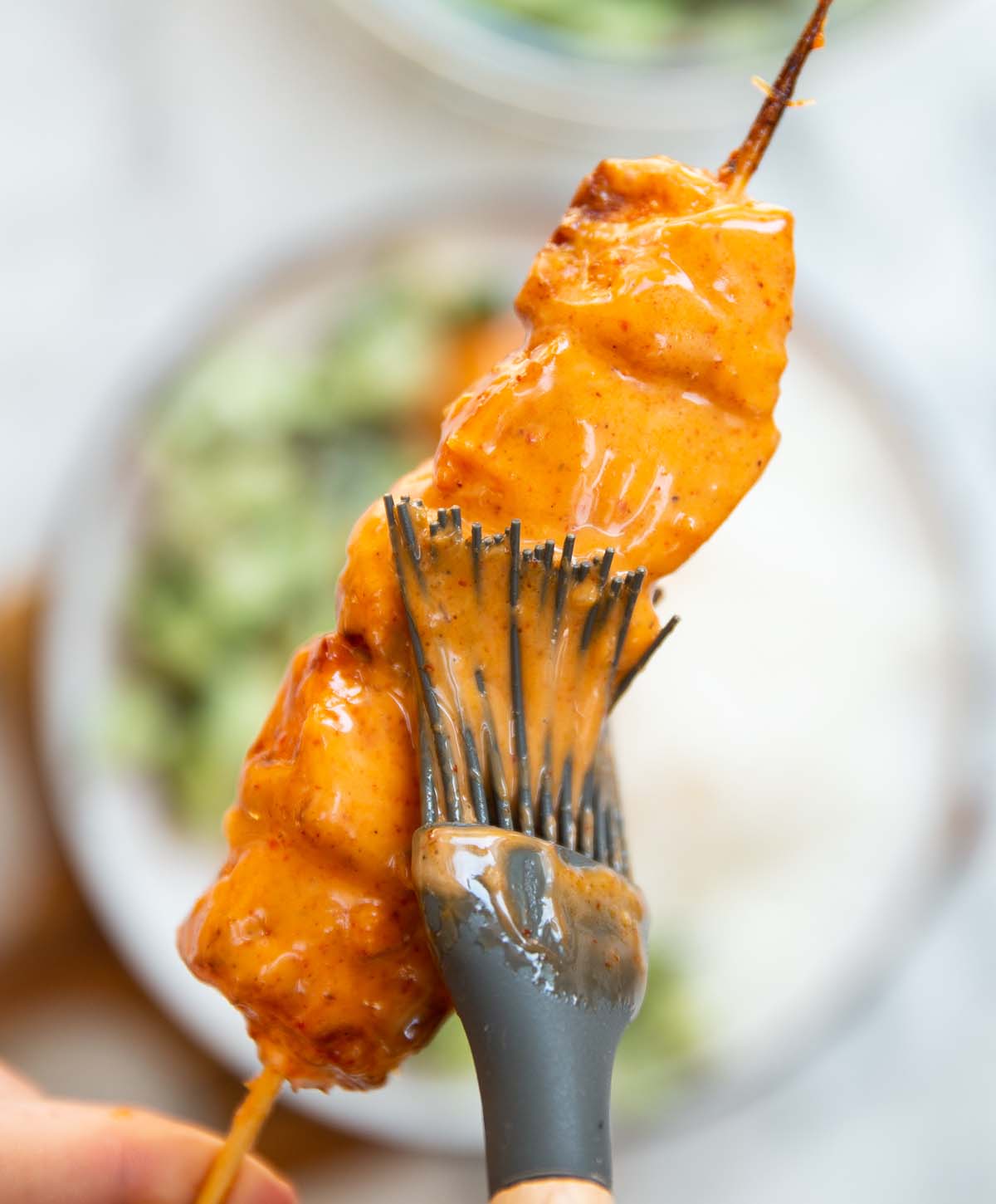 close up overhead shot of hand holding salmon skewers whilst brushing it with sauce