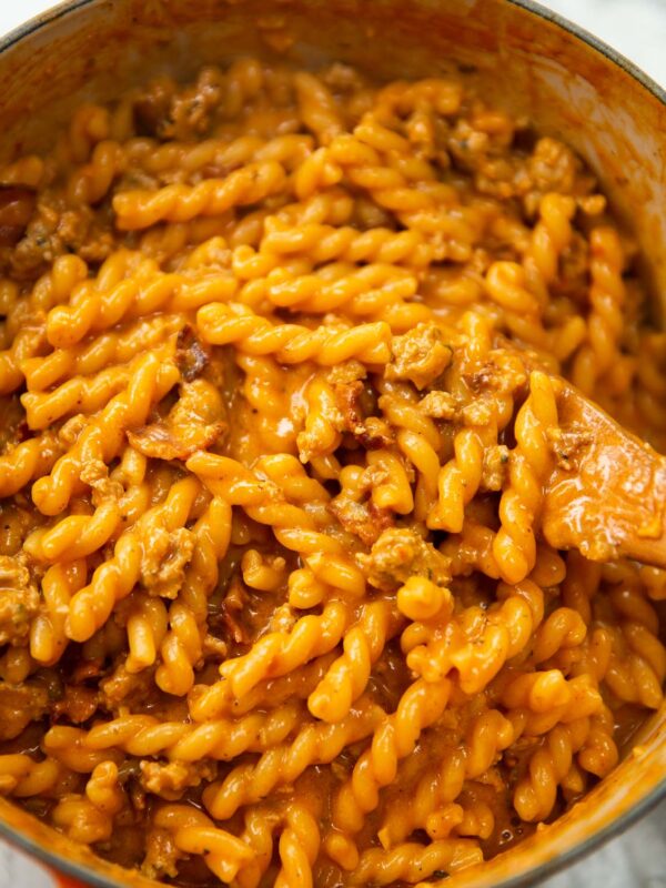 sausage and bacon pasta in large pot with wooden spoon digging in