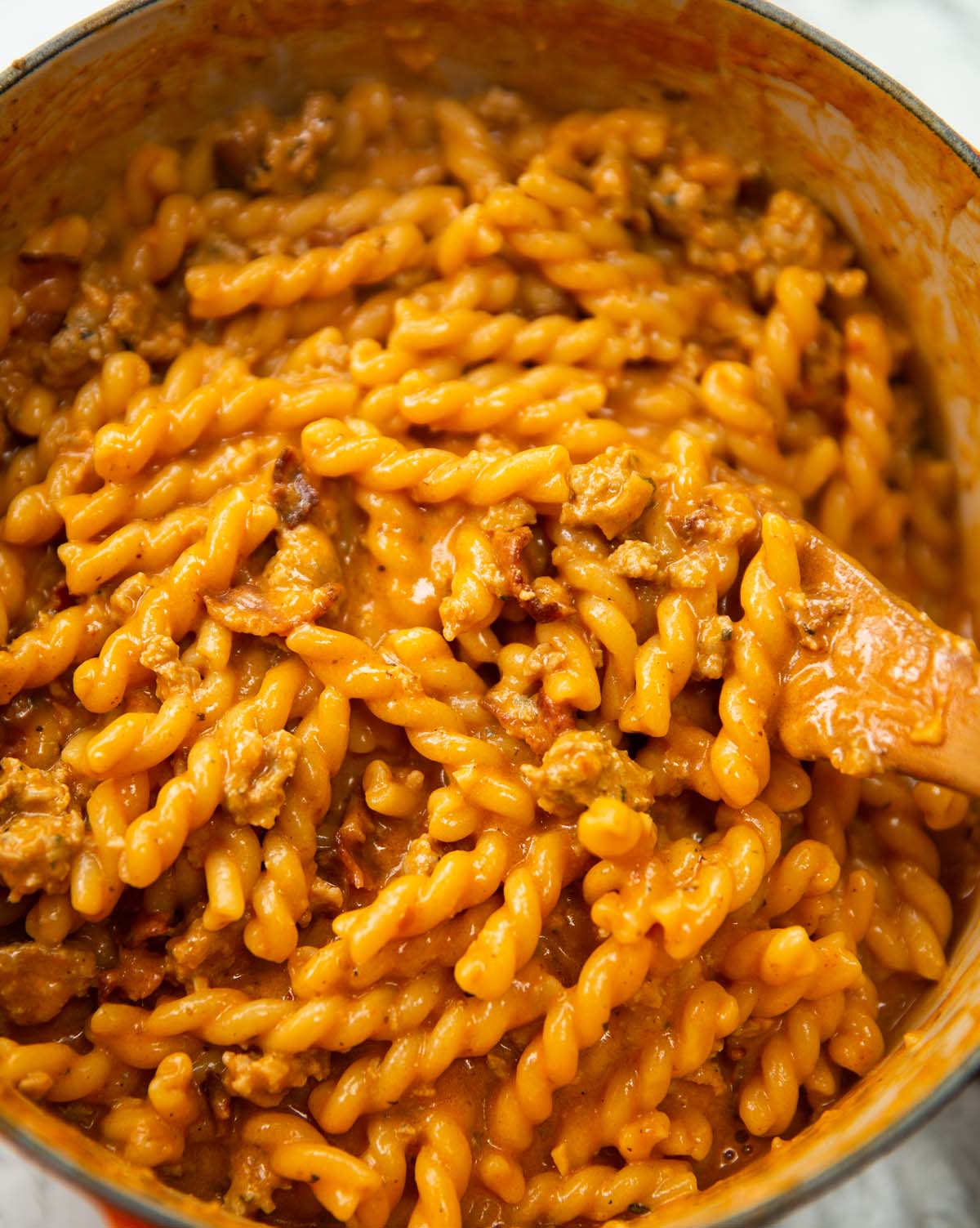 sausage and bacon pasta in large pot with wooden spoon digging in