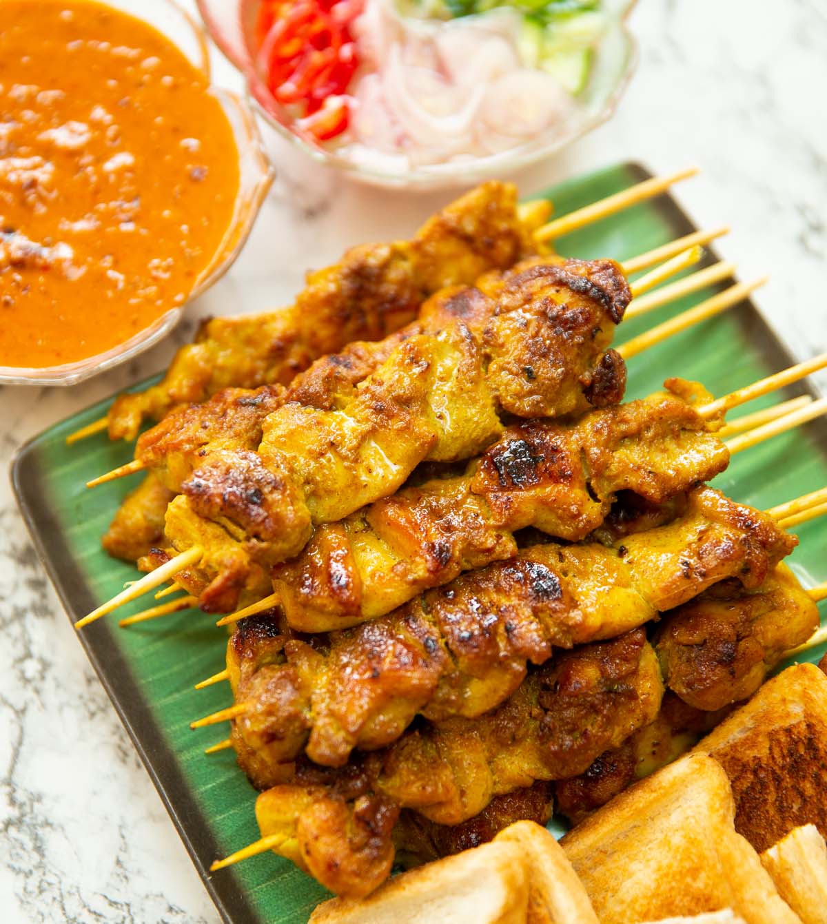 thai satay chicken skewers stacked on green board with dips next to them