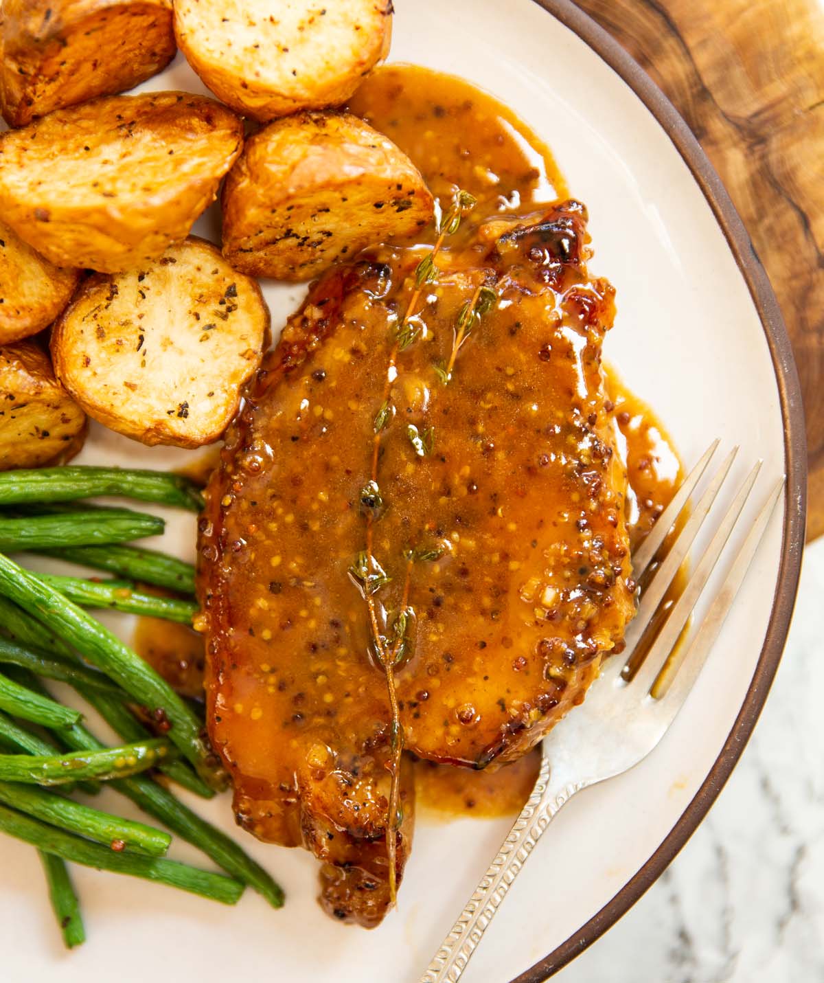 overhead shot of honey and mustard pork chop on small white plate with potatoes and green beans