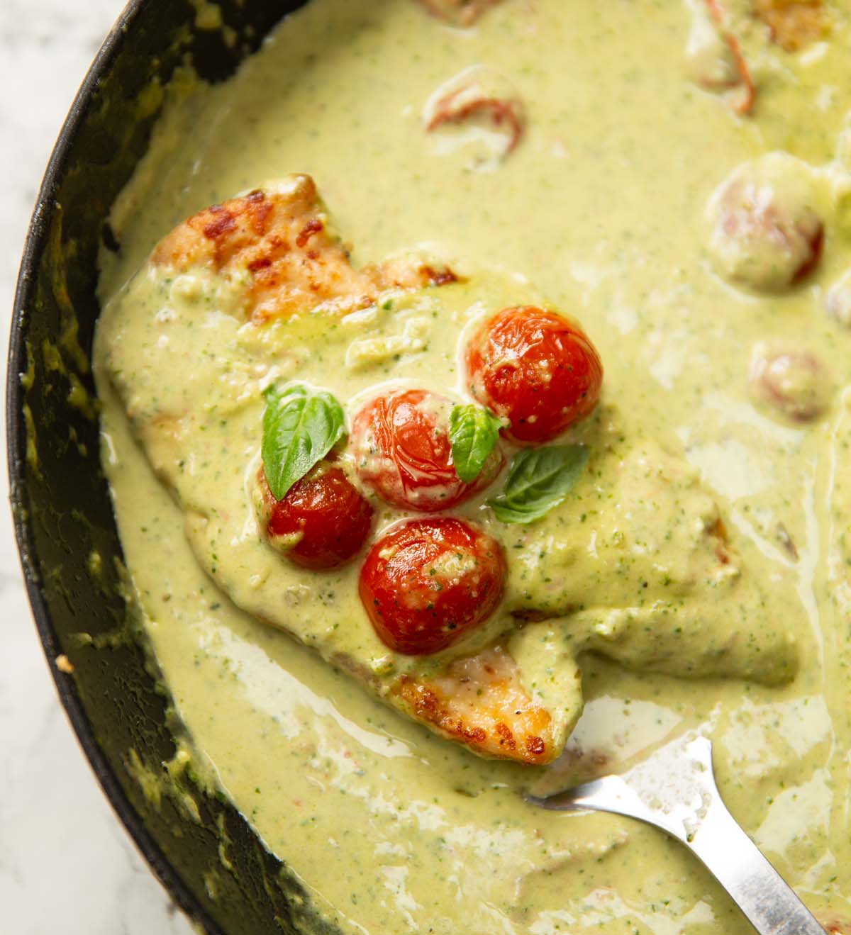 pesto cream chicken in pan with spatula digging in
