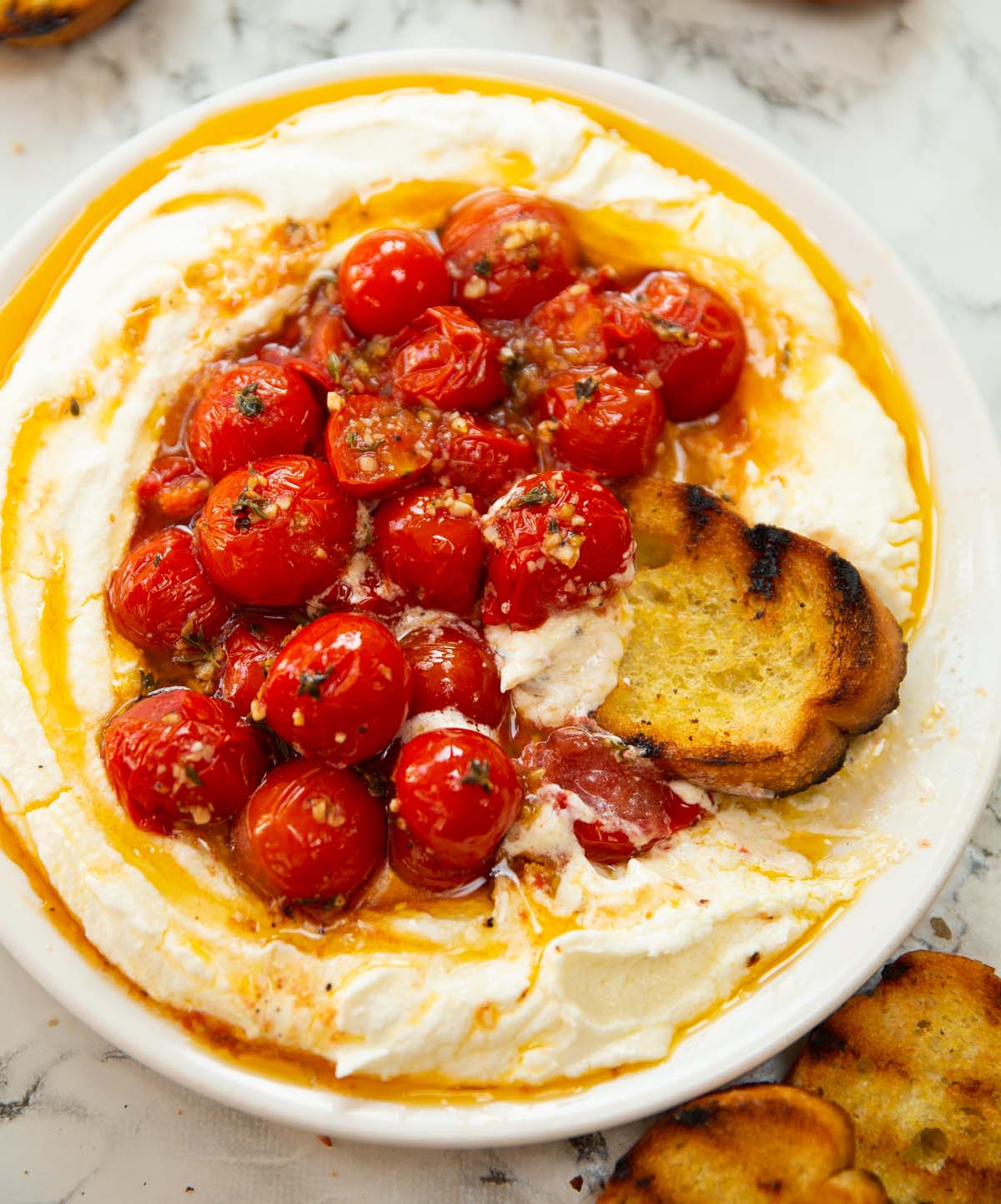 roasted tomatoes with whipped feta served on small white plate with toast dunking in