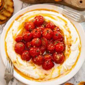 whipped feta roasted tomatoes on small white plate surrounded by toast