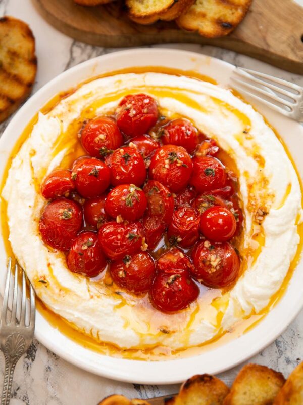 whipped feta roasted tomatoes on small white plate surrounded by toast