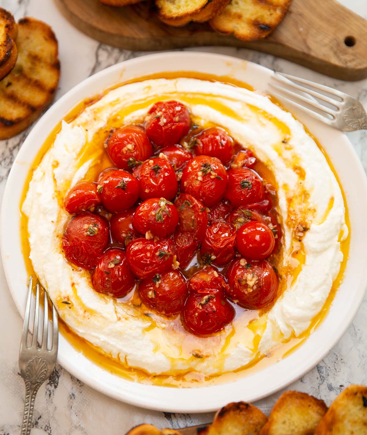 whipped feta roasted tomatoes on small white plate surrounded by toast