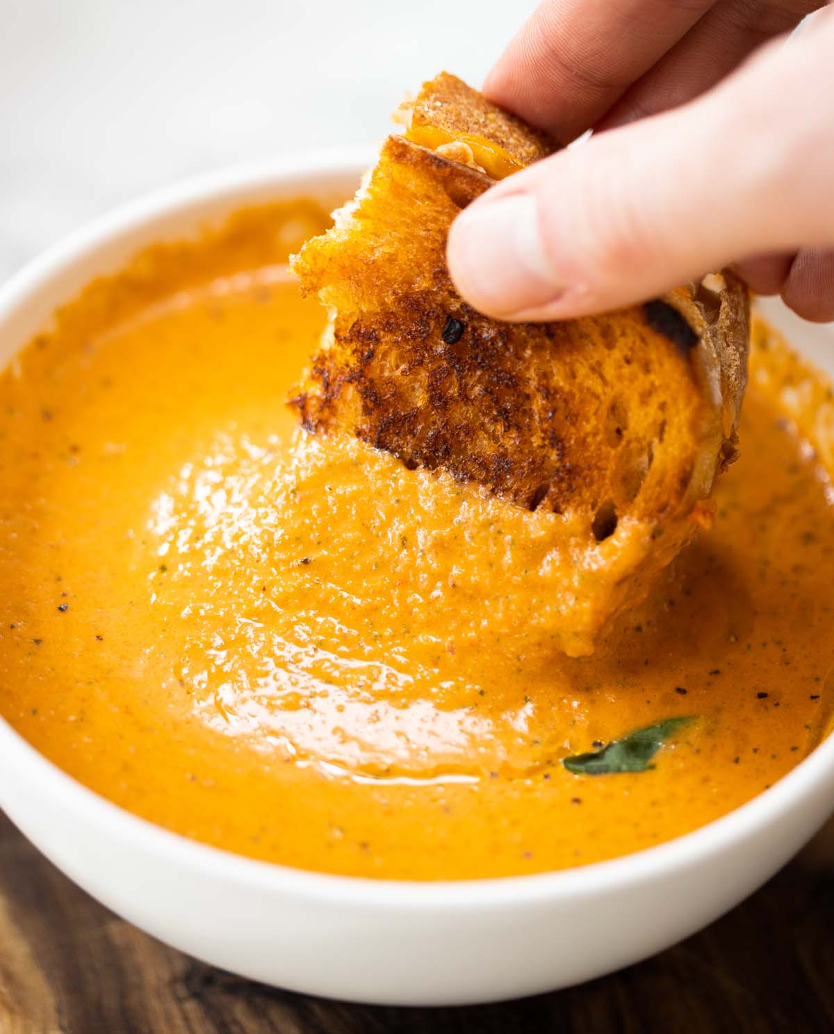hand dunking grilled cheese into small white bowl of soup