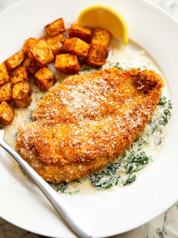 chicken and creamed spinach on white plate with potatoes and silver fork