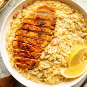 overhead shot of chicken bacon leek orzo in large white bowl with lemon wedges