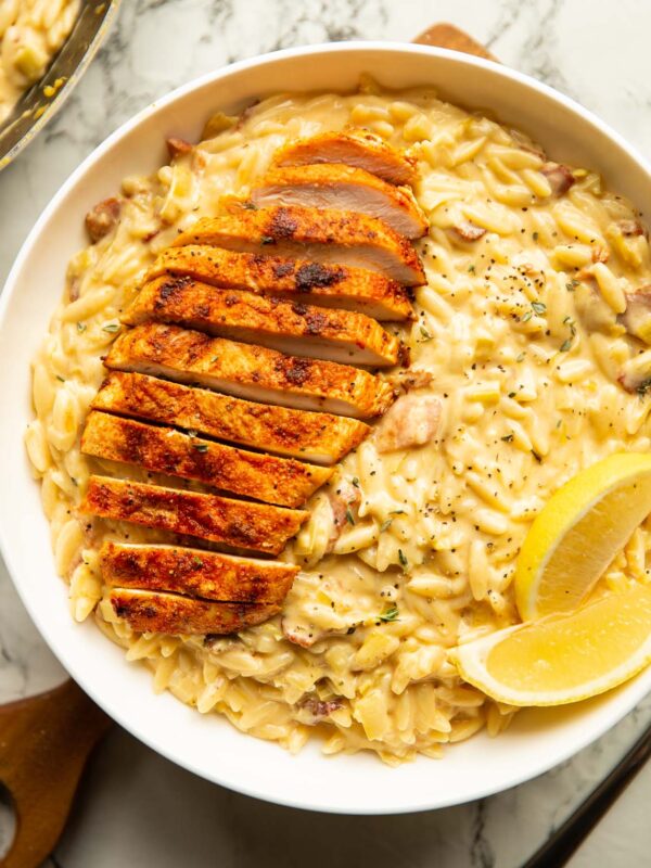overhead shot of chicken bacon leek orzo in large white bowl with lemon wedges