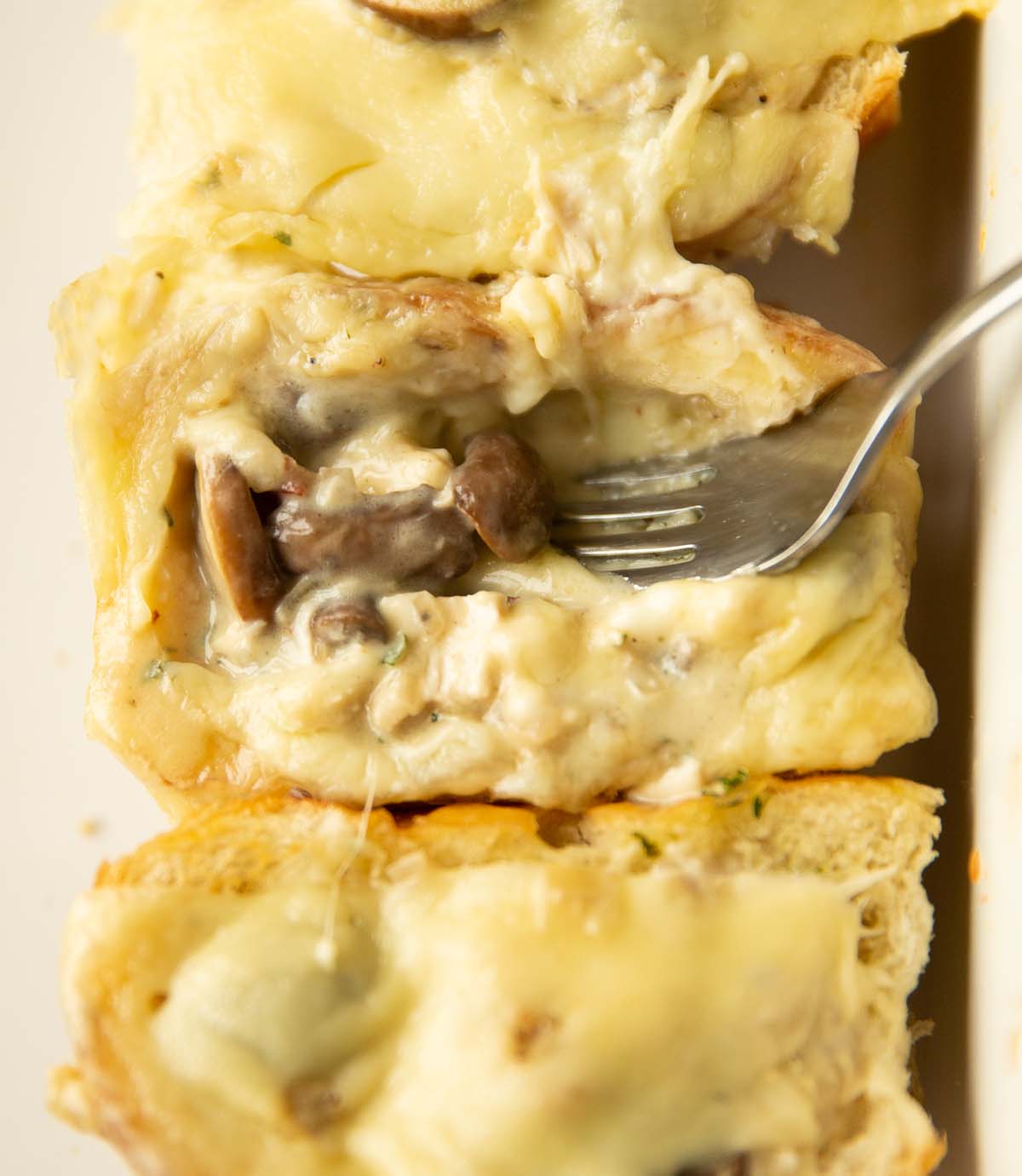 close up shot of silver fork digging into cheesy chicken mushroom slider