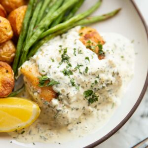 cod in parsley cream sauce on small white plate with baby potatoes and green beans