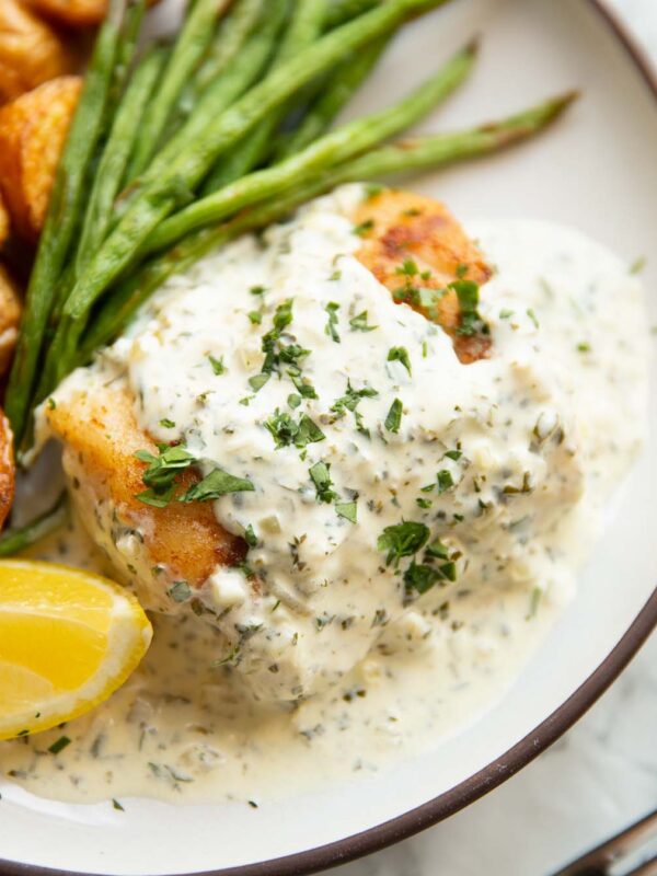 cod in parsley cream sauce on small white plate with baby potatoes and green beans