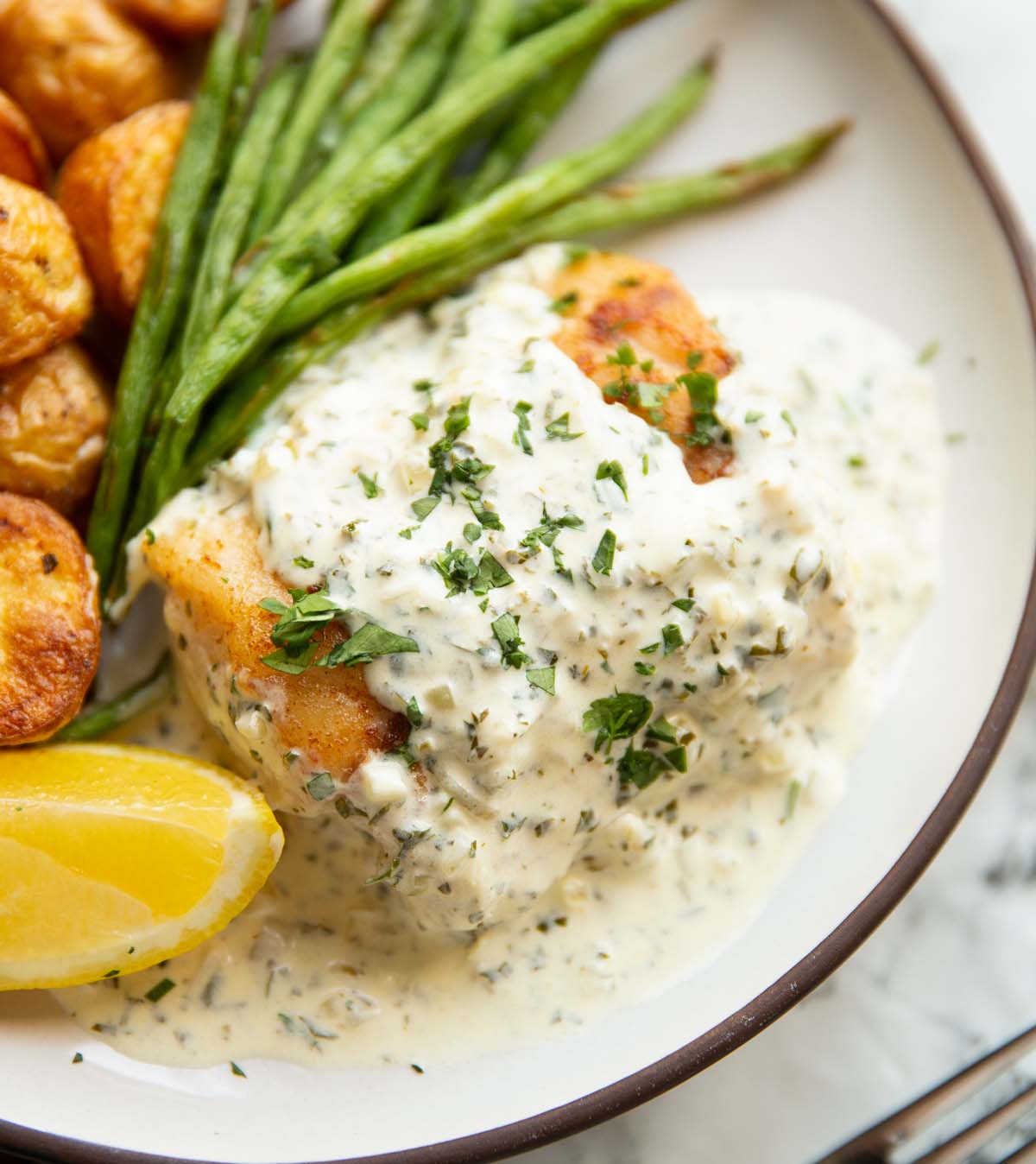 cod in parsley cream sauce on small white plate with baby potatoes and green beans