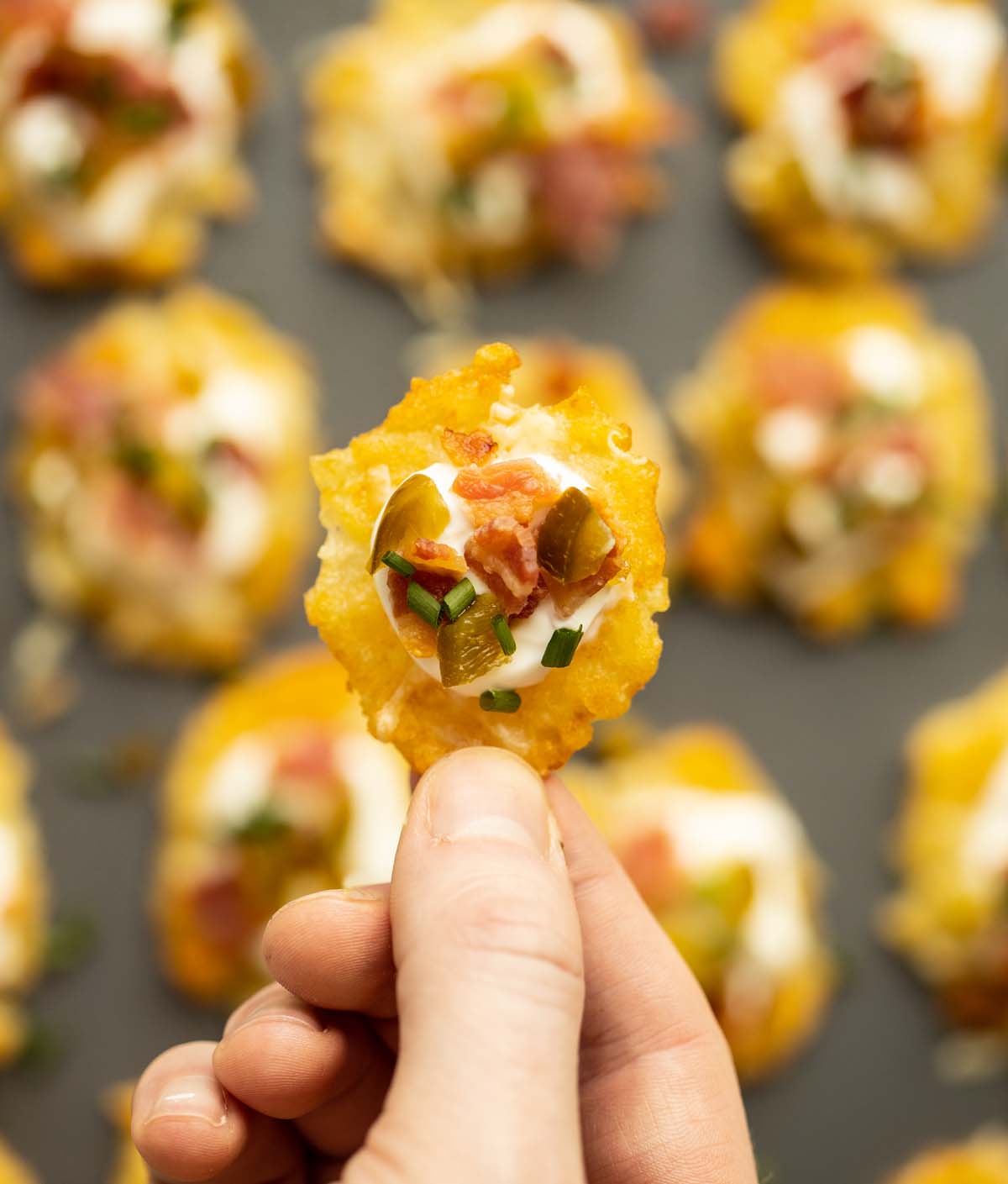 close up overhead shot of hand holding loaded tater tot above tray