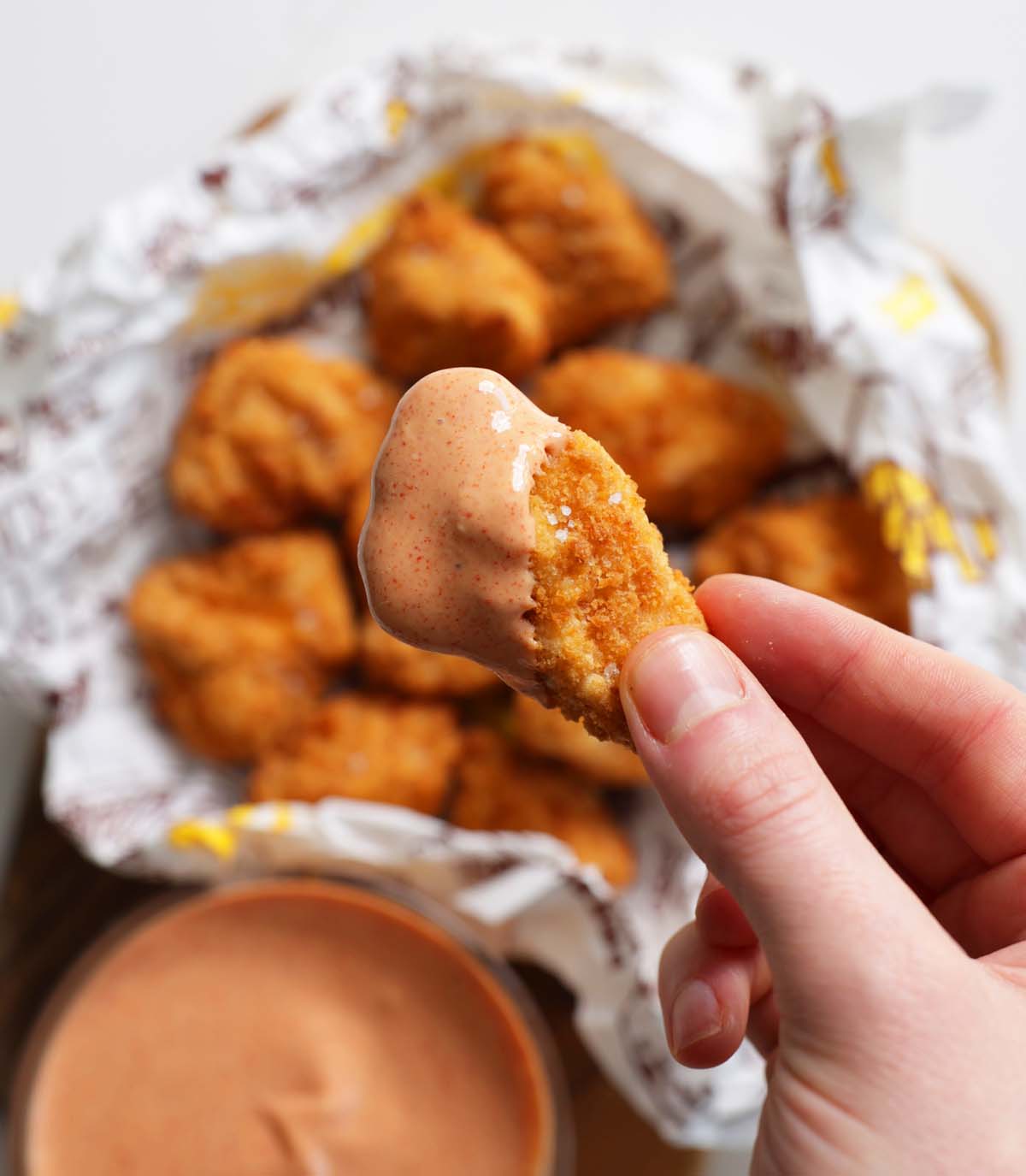 overhead shot of hand holding nugget with sauce dripping off it