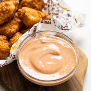 nugget dipping sauce in small glass bowl on wooden chopping board with nuggets blurred in the background