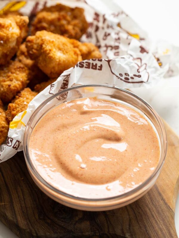 nugget dipping sauce in small glass bowl on wooden chopping board with nuggets blurred in the background