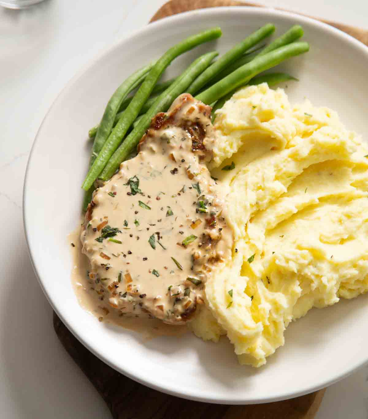 creamy dijon pork chop on small white plate with mash and green beans