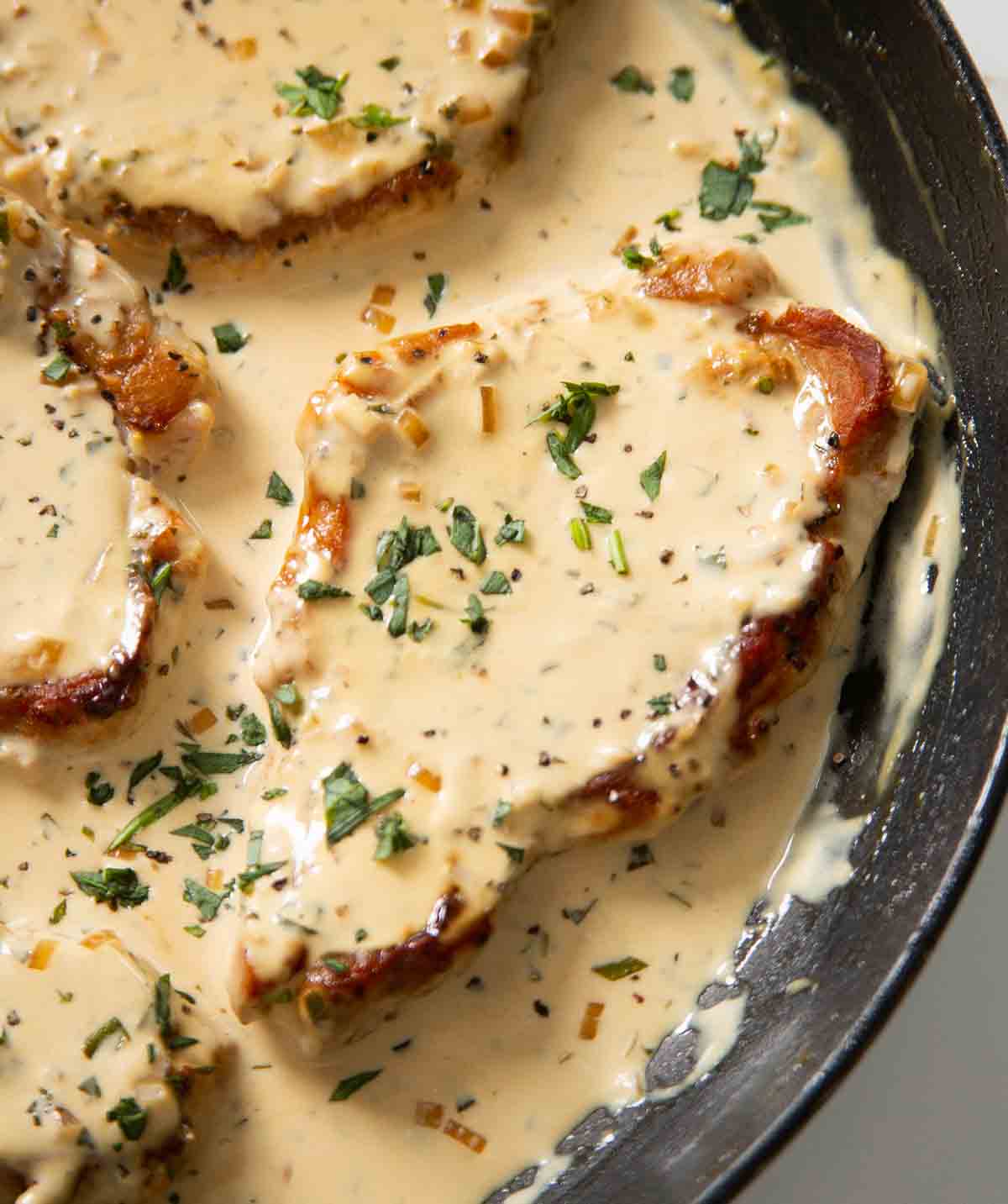 close up shot of pork chop in large pan garnished with tarragon