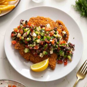 crispy greek chicken served on white plate with wedge of lemon